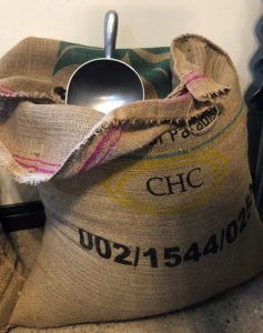 Burlap sack of green coffee beans with a steel scooper.